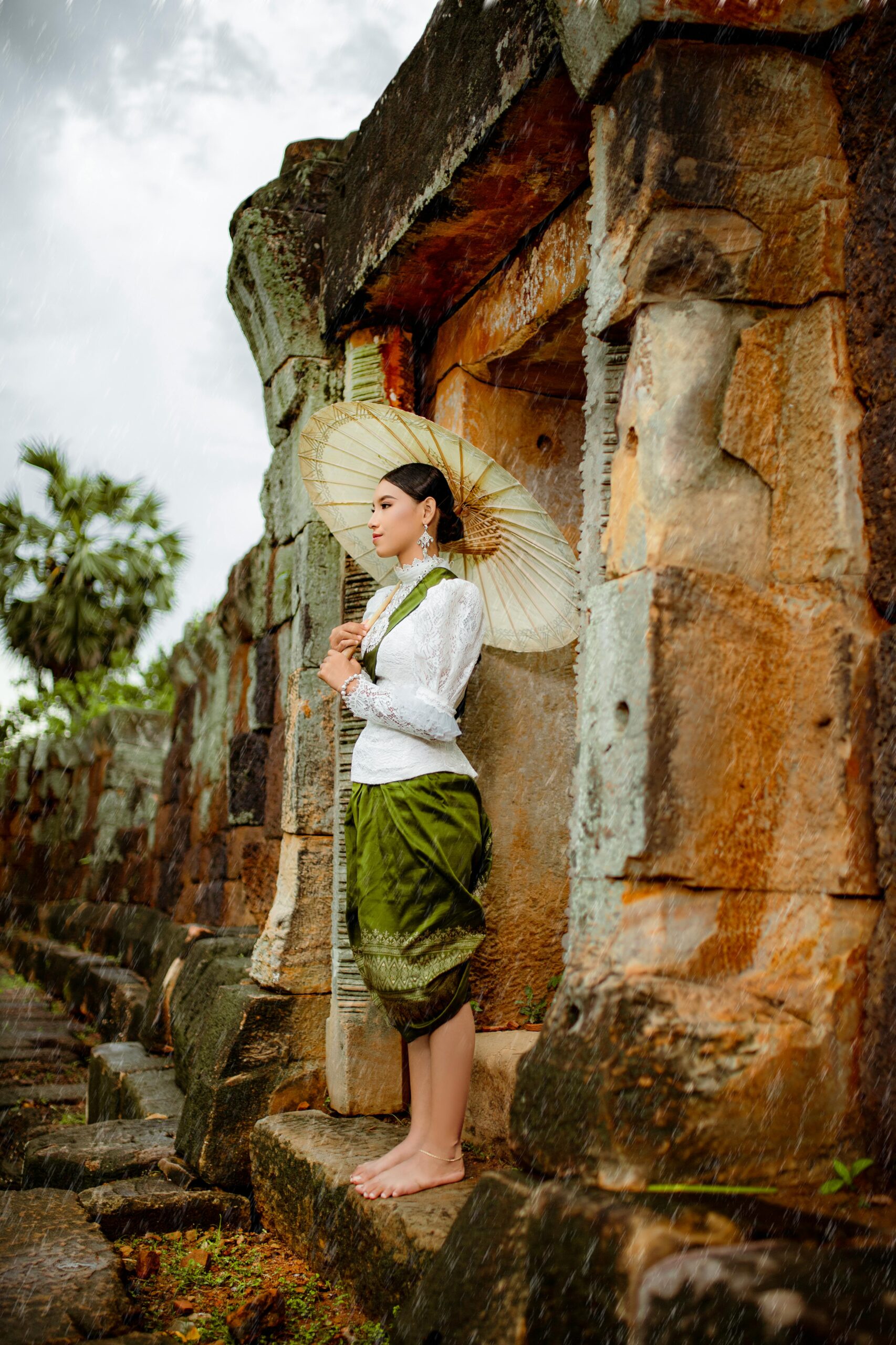 Woman in traditional Khmer clothing with umbrella at ancient Cambodian ruins.