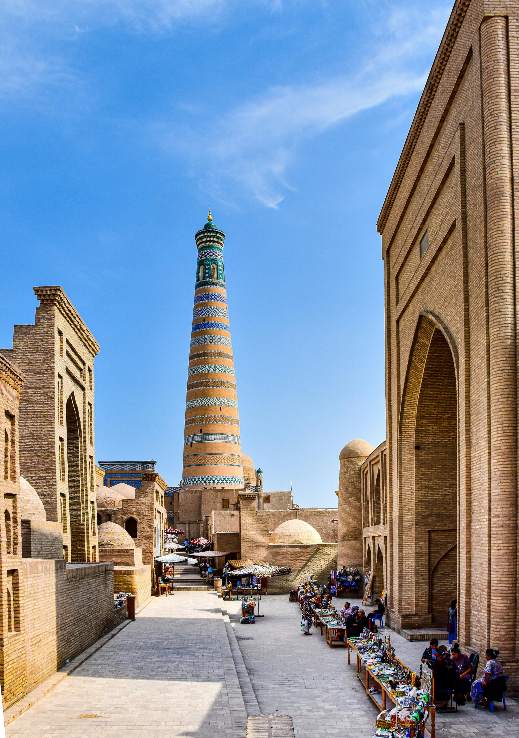 The historic Islam Khoja minaret and its surrounding architecture under a bright blue sky in Khiva, Uzbekistan.