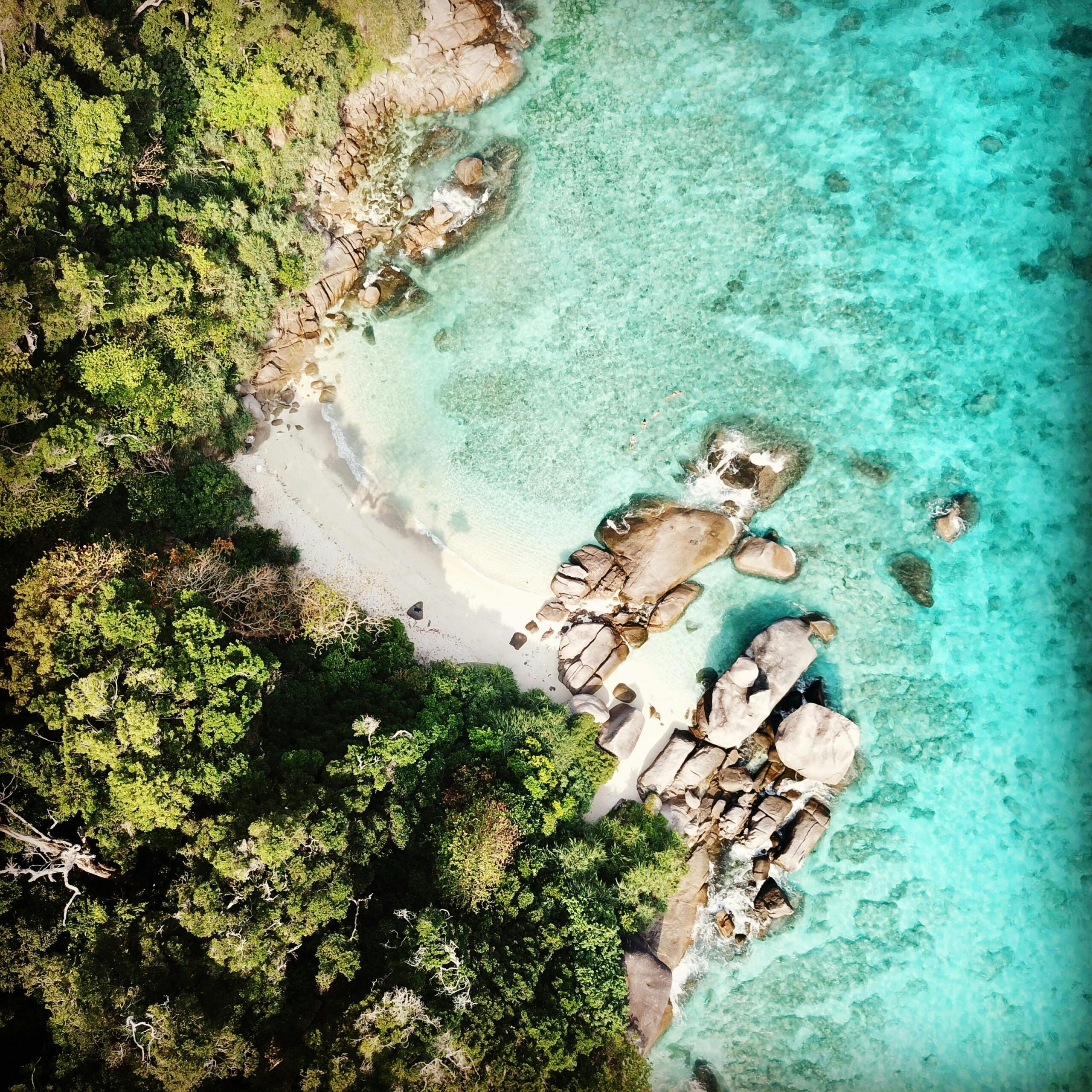 A stunning aerial shot of a turquoise beach with rocks and lush greenery in Thailand.