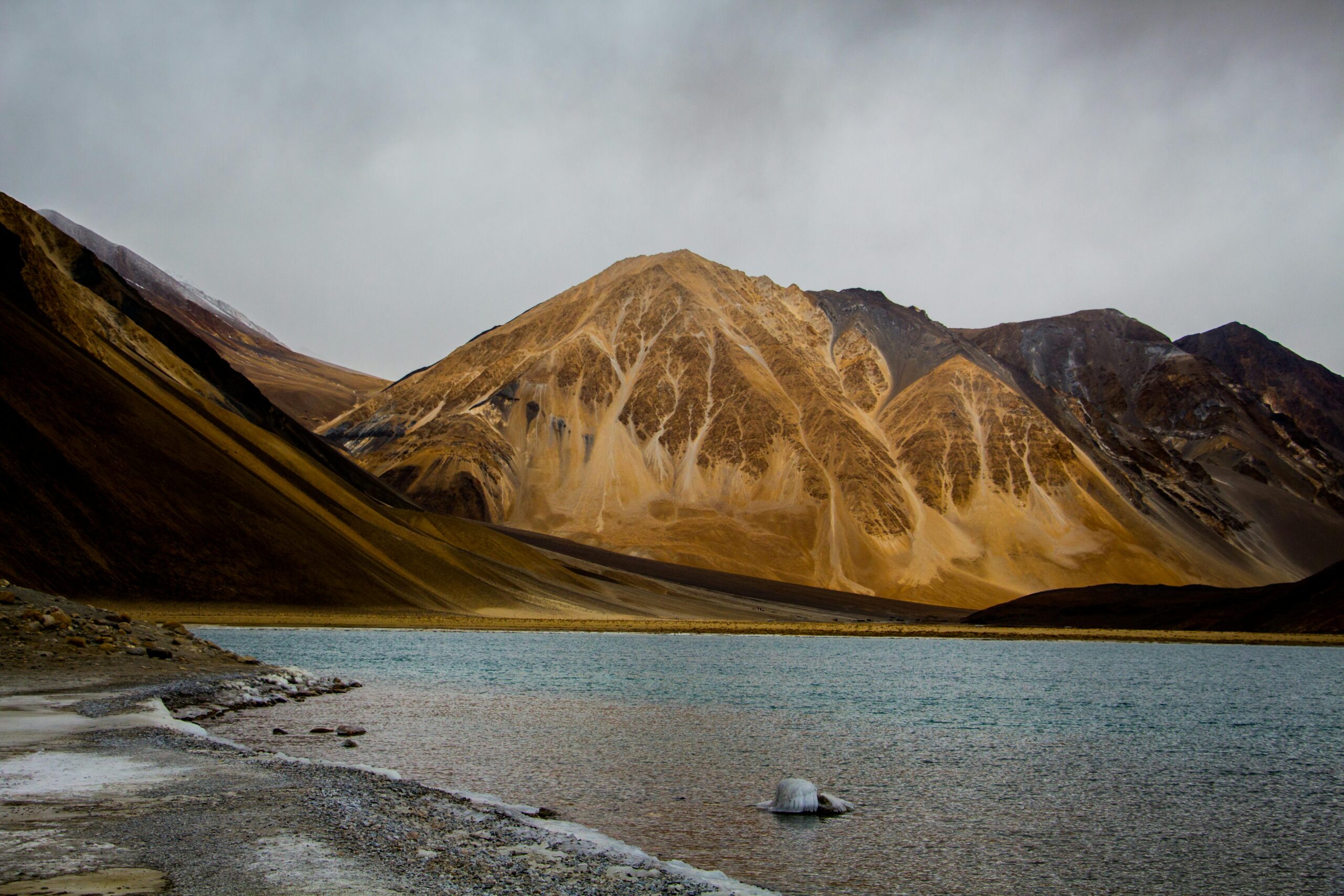 Majestic view of Pangong Lake with surrounding mountains under cloudy skies in Leh, India.